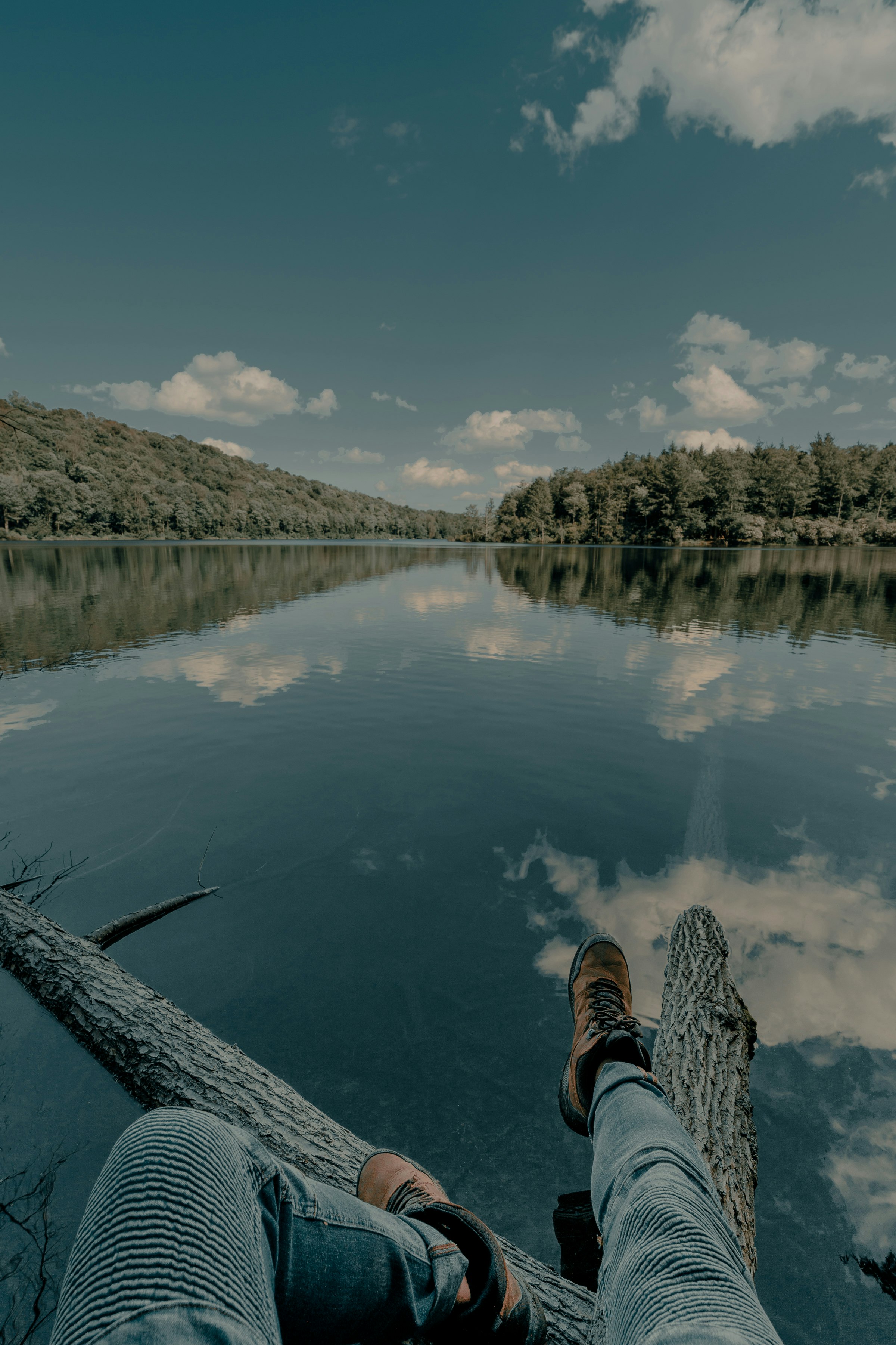 person in black and white sneakers sitting on wooden dock over the river during daytime